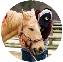 A person wearing a UNC hat and petting a horse